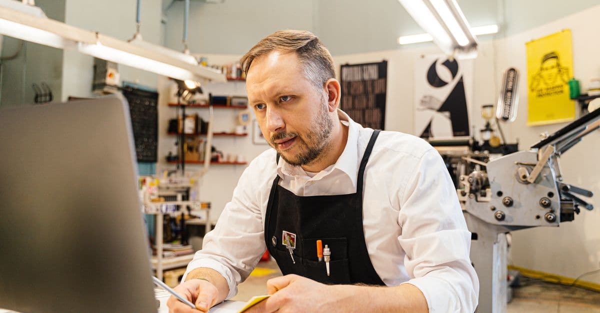 A New Zealand small business owner working at a computer in his shop, the kind of owner who manages his own online listings