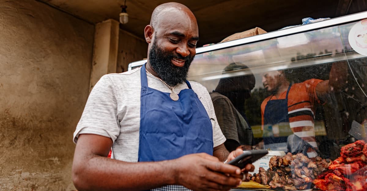 A New Zealand small business owner in an apron checking their phone at their shopfront, the kind of owner who manages their own Google Business Profile