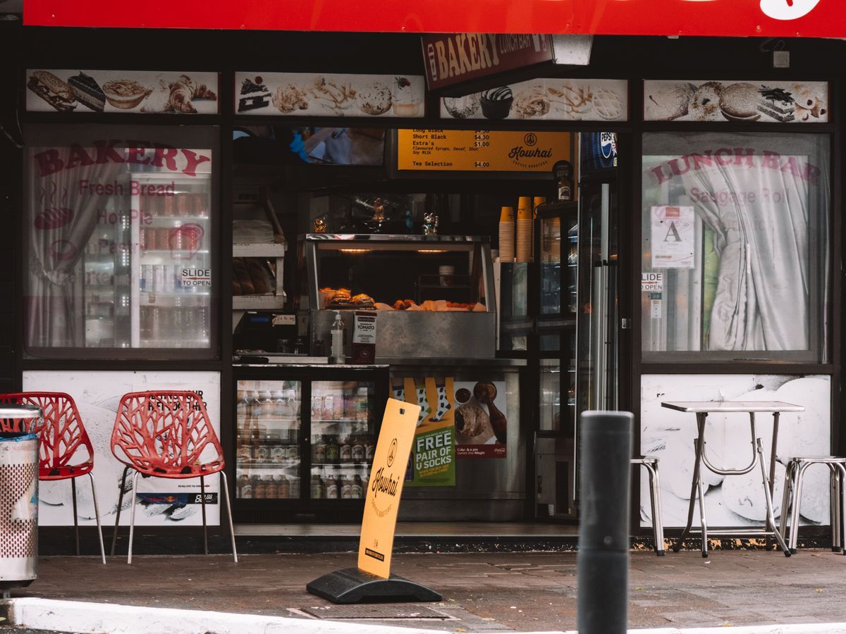 A classic Kiwi bakery and lunch bar storefront in Auckland, with hot pies in the cabinet and chairs on the footpath